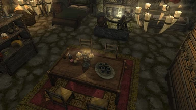 Main living area showing large bed, fireplace, small bed, weapon racks, and table.
